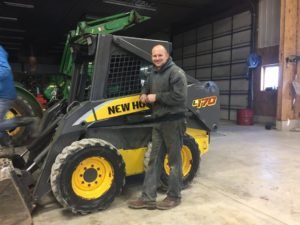 Brad, founder of AftermarketTractorParts.com, standing next to a New Holland skid steer in his shop